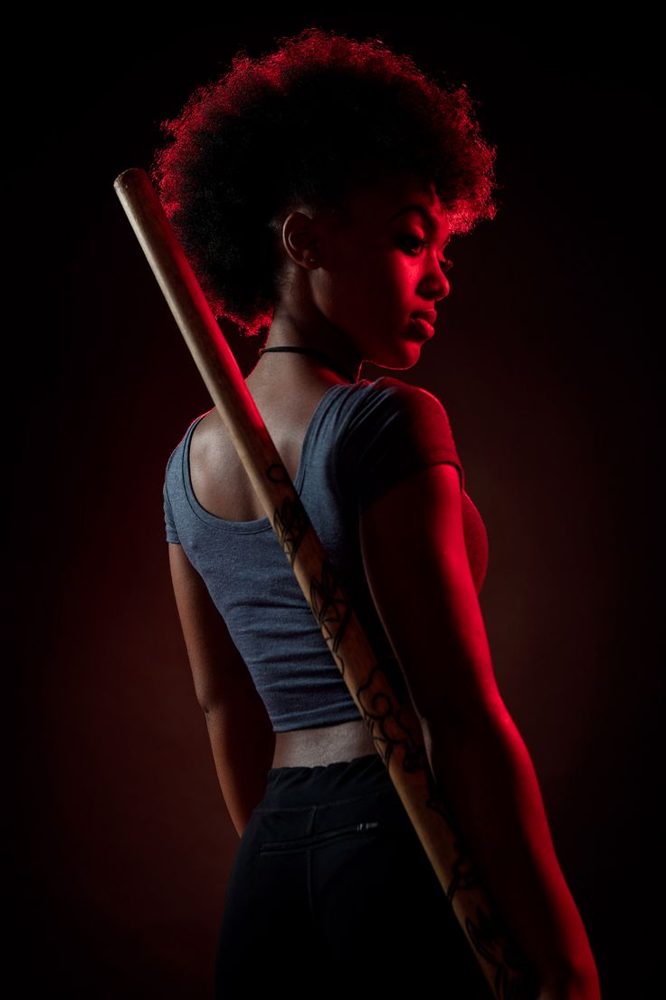 a woman with an afro  posing with a wooden stick, with red lighting. she looks serious and strong.