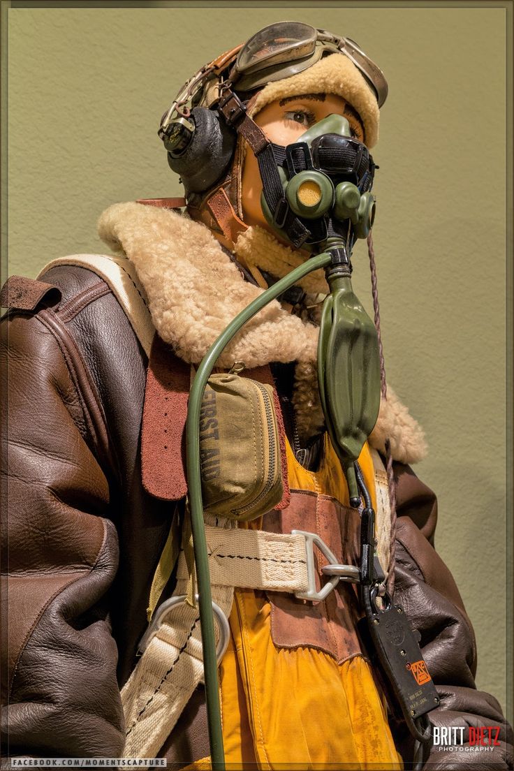 the image showcases a detailed closeup of a meticulously preserved world war iiera pilot's flight suit.  the mannequin is wearing a brown leather a2 flight jacket with a sheepskin collar,  goggles, and an oxygen mask with a respirator.  a parachute harness and a small firstaid kit are visible on the vest.  the overall condition suggests the suit is a museum exhibit or carefully preserved historical artifact, representing the attire and equipment of a pilot during the world war ii era. the background is a muted, neutral green. the lighting is carefully controlled, highlighting the texture and details of the clothing and equipment.