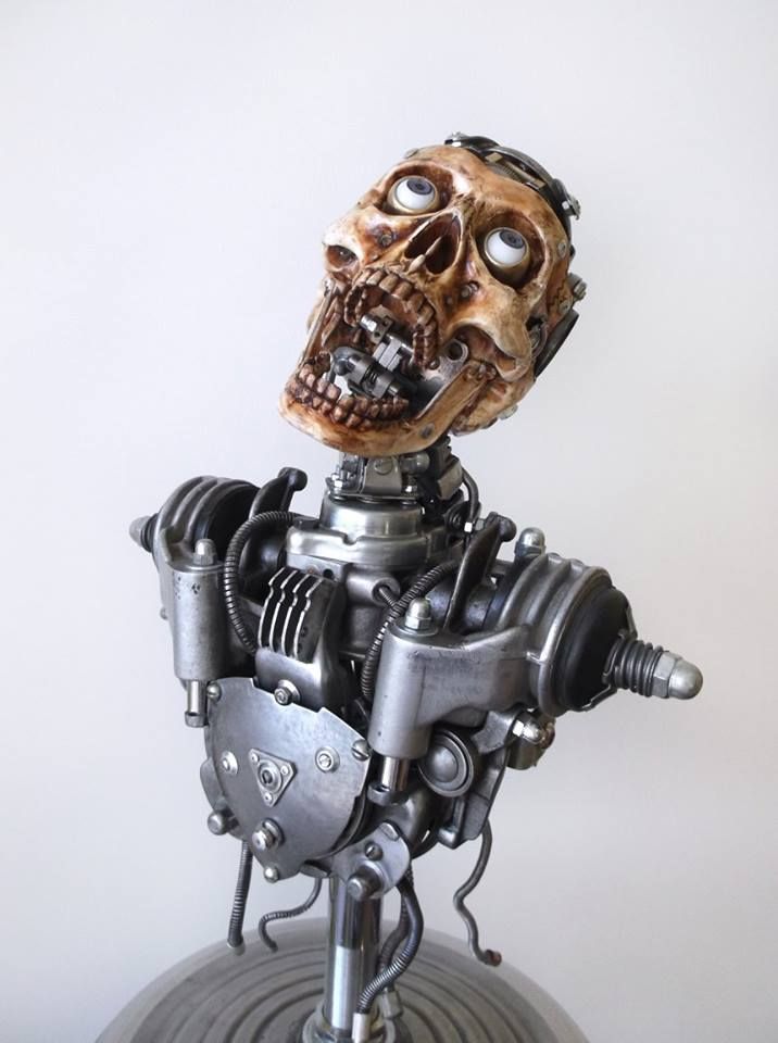 a closeup shot of a steampunkstyle robot sculpture. the robot is made of metal gears, wires, and pipes. the head is a skull with large, white, bulging eyes. the sculpture looks very detailed and intricate and is a very cool example of a work of art made from recycled materials.