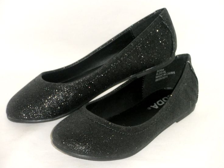a pair of women's black glittery ballet flats are displayed on a white background. the shoes are overlapping. one shoe is angled towards the upper left while the other sits at the lower right. the brand name "moda" is partially visible on the insole of the lower shoe.