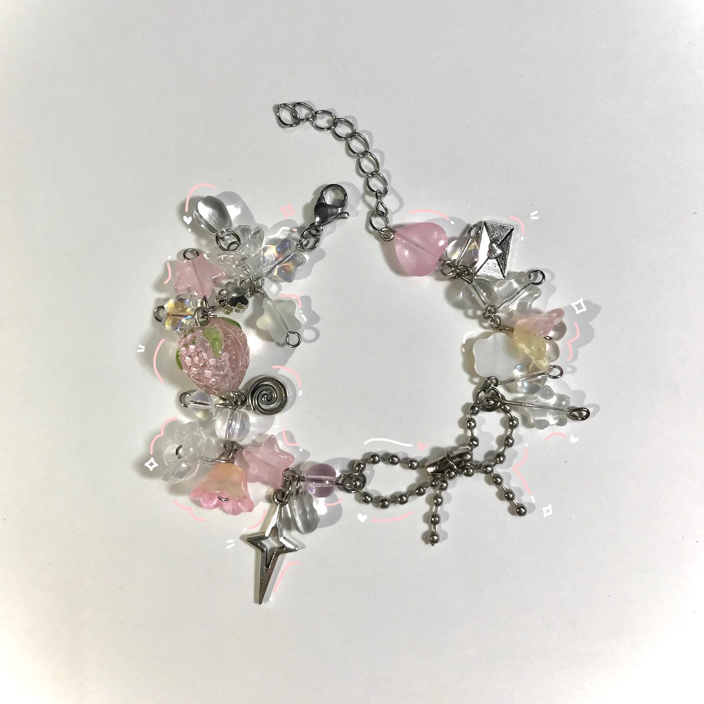 a handmade charm bracelet featuring an assortment of pink, clear, and silver beads and charms. charms include a strawberry, star, and flowers. the bracelet has a silver chain and clasp.
