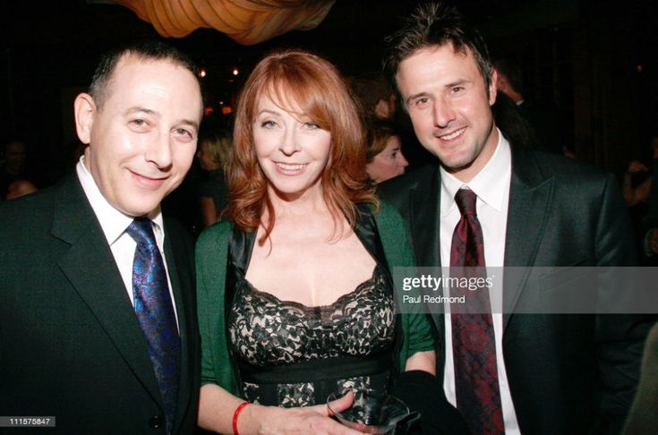 a photo of three celebrities, dressed in formal wear. they are all smiling and posing for the camera. the woman in the center is wearing a green jacket over a black and white lacy dress. the man on her left is wearing a black suit with a blue tie. the man on her right is wearing a black suit with a red tie.