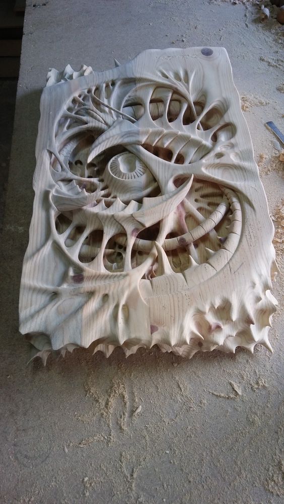 a closeup shot of an intricately carved wooden sculpture. the sculpture is abstract and organic in form, featuring a complex interplay of curves, lines, and textures. it appears to be made from lightcolored wood, and the carving is highly detailed, showing the skill and precision of the artist. the sculpture is resting on a work surface, and there is sawdust visible around it, indicating that it is likely a work in progress. the overall style of the sculpture suggests a contemporary approach to wood carving, combining natural forms with a sense of movement and energy.