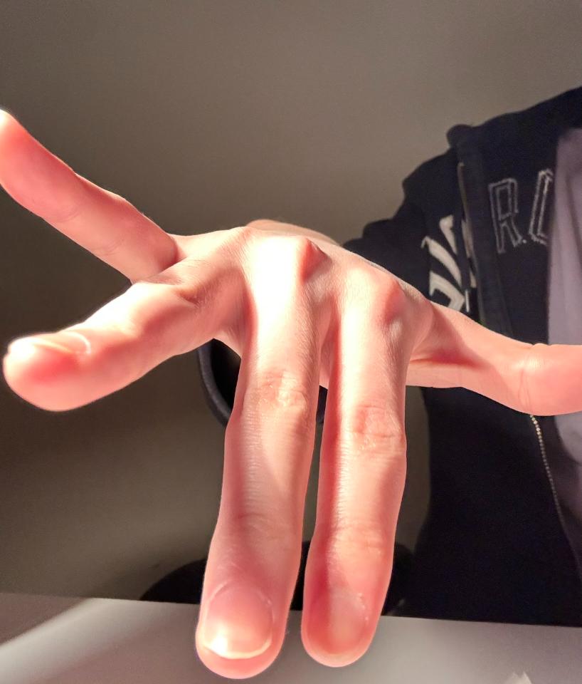 a closeup image of a hand reaching towards the camera. the hand is illuminated by artificial light, creating strong shadows and highlights. the fingers are slightly spread apart, as if in motion. the background is blurry and out of focus, drawing attention to the hand in the foreground.