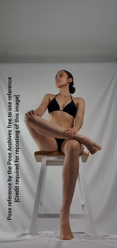 a woman in a black bikini is sitting on a white stool with her right leg crossed over her left leg. she is looking up and to the left. the background is a white sheet. the image is a pose reference for artists.
