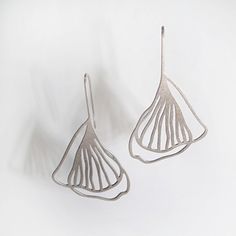 a closeup shot of two silver earrings on a white background. the earrings are shaped like ginkgo leaves and have a minimalist design. they are both delicate and elegant, and would be perfect for any occasion.