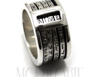 a closeup shot of a silver ring with a unique design. the ring features a rotating band with multiple rows of engraved letters, creating a cipherlike effect. the ring's surface is polished, adding to its sleek and elegant appearance. the band is thick and substantial, showcasing the craftsmanship involved in its creation. this ring is a perfect accessory for anyone looking for a unique and stylish piece of jewelry.
