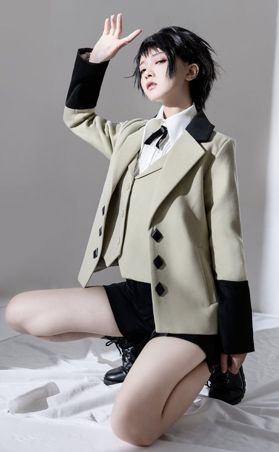 young woman in a stylish, androgynous suit strikes a pose in a brightly lit studio. the low camera angle emphasizes her confident posture. the suit features a unique blend of masculine and feminine elements, including a doublebreasted blazer, a crisp white shirt, and tailored shorts. her dark hair is styled in a chic, short cut, and her makeup is minimal, highlighting her natural features.