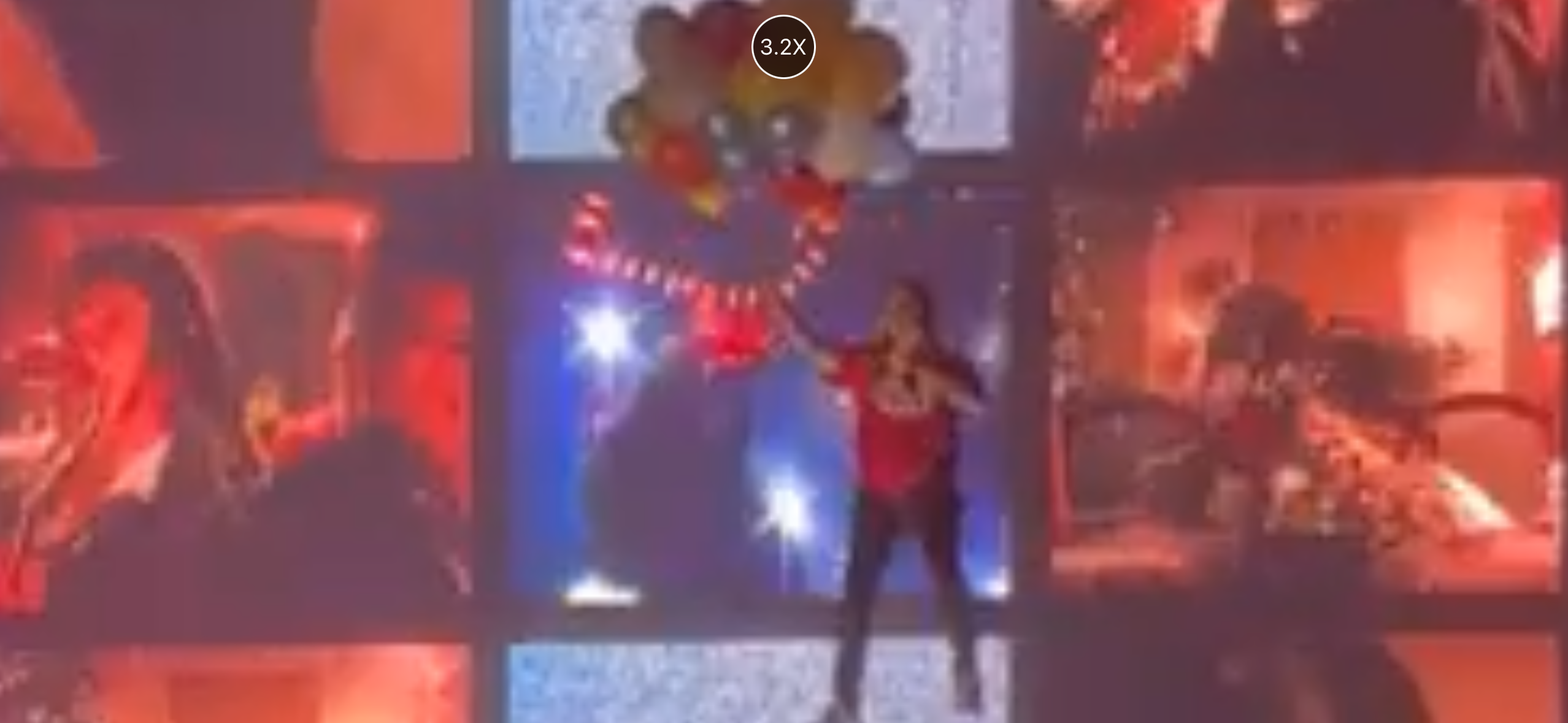 a woman in a red shirt performs on a stage lit with red spotlights. the background is decorated with balloons and confetti.