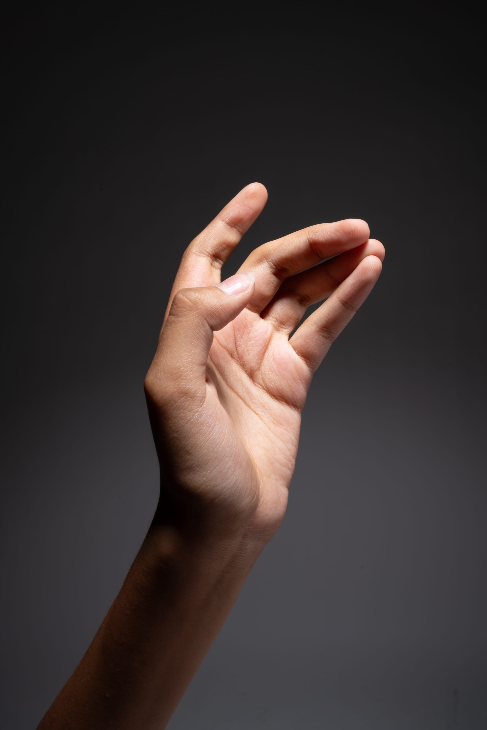 a left hand of a person is extended with fingers spread out against a gray background.  the light comes from the upper left direction.