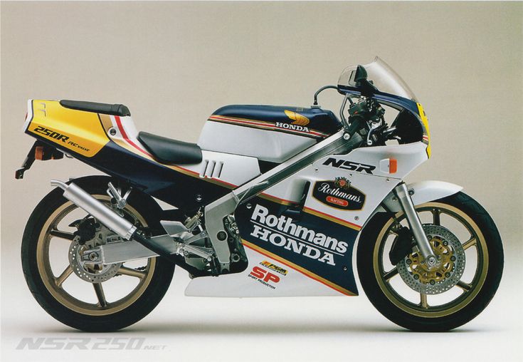 a closeup shot of a honda nsr250r race bike with the rothmans livery from the early 1990s. the bike is a twostroke, 250cc machine.  the bike is shot from a slightly low angle.