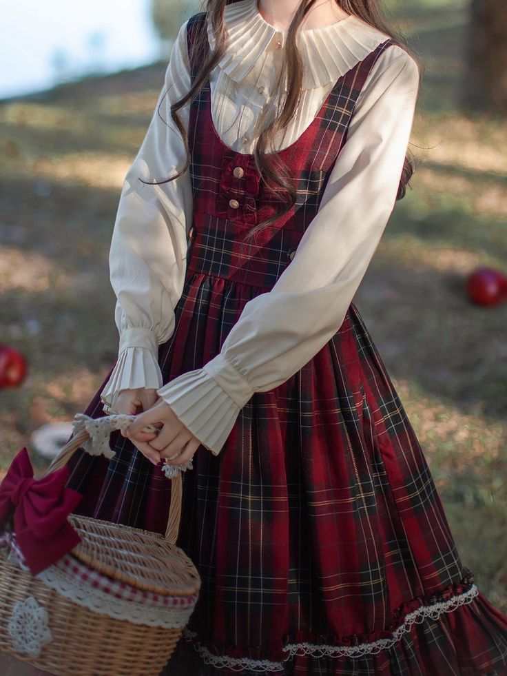 a woman in a red and black plaid dress and a white blouse stands in a forest holding a picnic basket.
