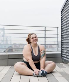 a woman in workout clothes is sitting on a deck stretching her legs. she is smiling and appears to be happy with her workout.
