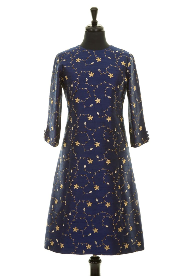 a blue silk dress with gold embroidery, standing on a mannequin. the dress has a floral design and 3/4 sleeves. the mannequin is on a white background.