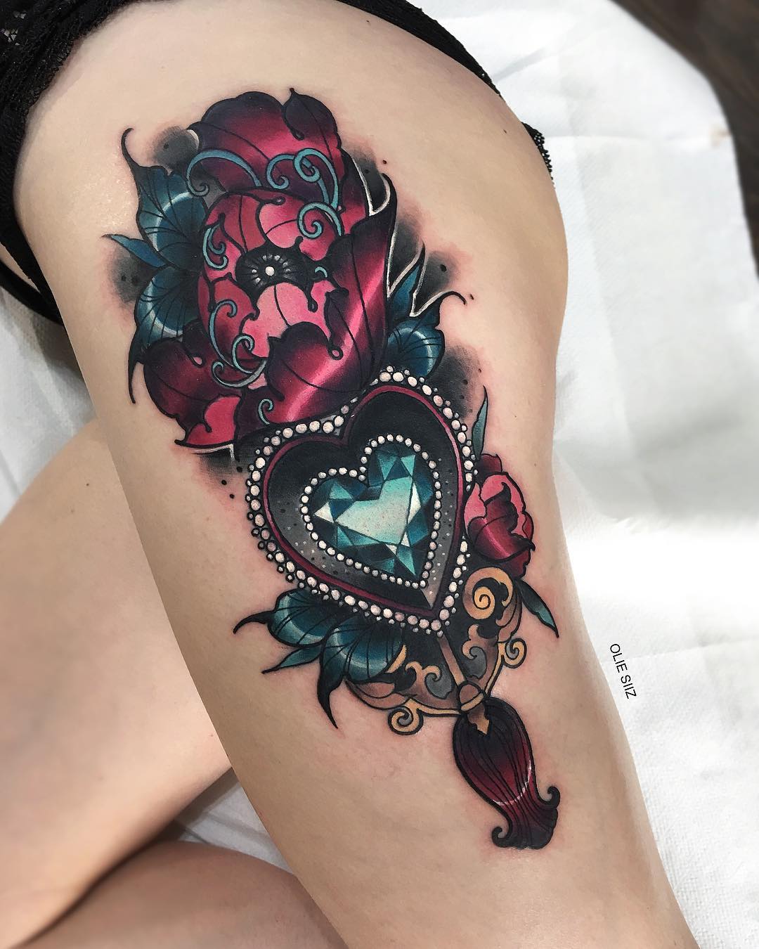 a neotraditional style tattoo on someone's upper thigh. the tattoo depicts a red flower with an ornate heartshaped key dangling from it. there is a blue jewel in the center of the heart. the tattoo has shading that makes it appear threedimensional.