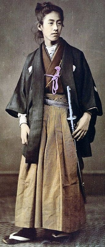 a colorized portrait of a young samurai stands in traditional attire, holding a katana sword. he wears a layered kimono with a hakama (widelegged trousers) and a haori (hiplength jacket). his hair is styled in a topknot, a common hairstyle for samurai during that era. the soft lighting and neutral background create a sense of quiet intensity and dignity.