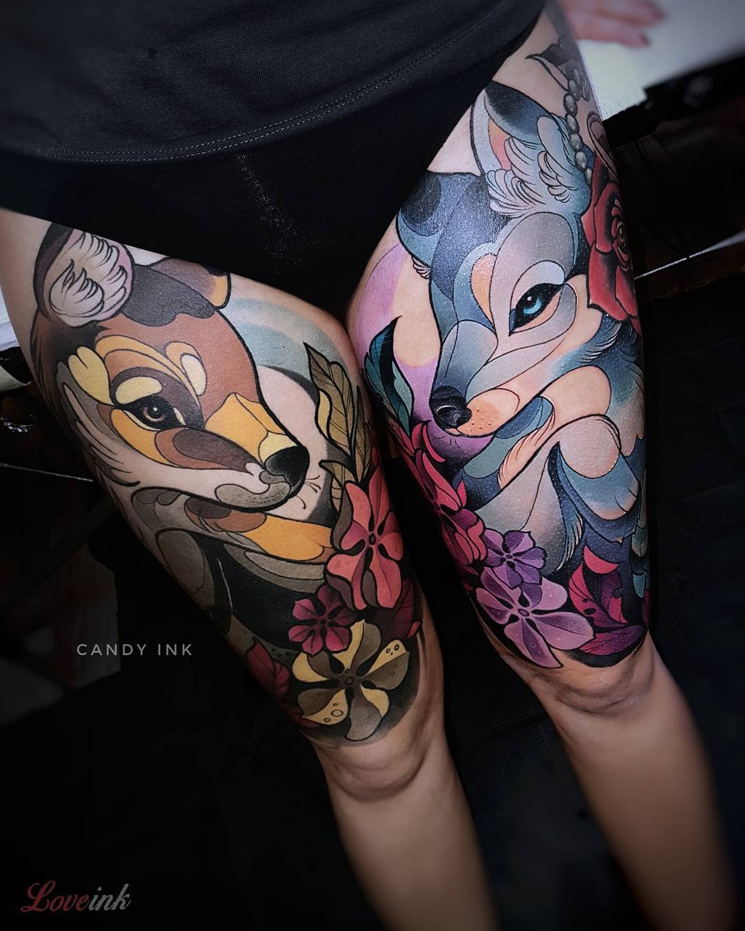 the image showcases a pair of vibrant neotraditional tattoos inked on a woman's thighs. the tattoos depict a stylized fox and wolf, each adorned with colorful floral arrangements. the fox, rendered in warm hues of orange and yellow, graces the left thigh, while the wolf, depicted in cool blues and purples, adorns the right. the intricate details and bold colors of the tattoos create a striking visual impact.