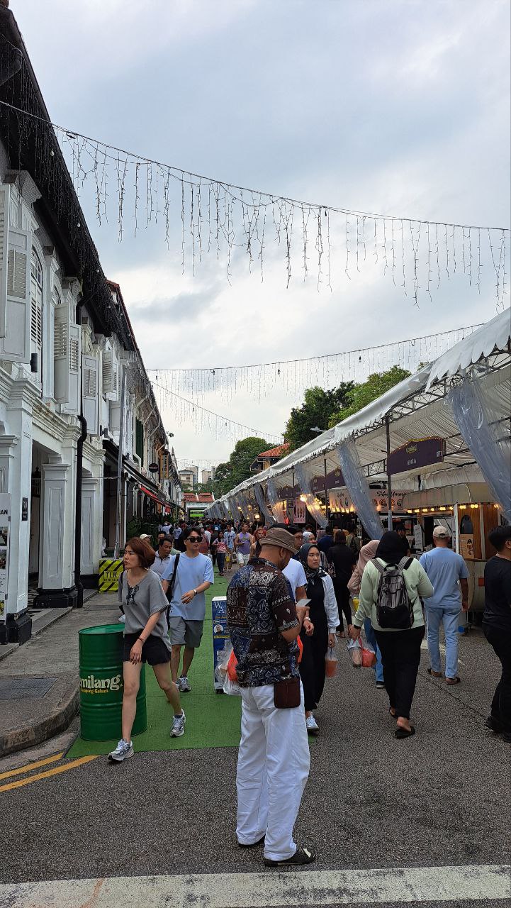 an image of a bustling street market in singapore. the street is lined with stalls selling a variety of goods and food. there are many people walking around, shopping and browsing. the market is located in a historic district of singapore, and the buildings are old and traditional. the atmosphere is lively and bustling, and there is a sense of excitement and energy.