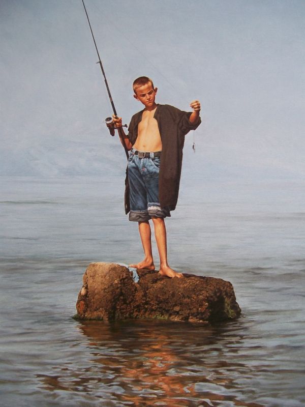 a young boy stands barefoot on a rock in the middle of the water, holding a fishing rod. he's wearing denim shorts, an open dark shirt, and looks at the fishing line in his hand. the ocean surrounds him, and the sky is overcast.