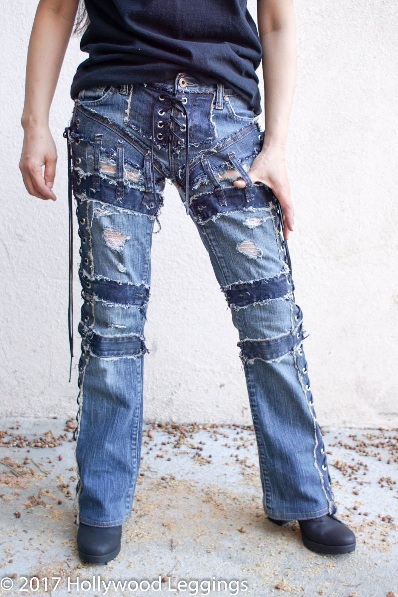 a woman is wearing a pair of light blue denim jeans that are ripped, distressed, and have lace up sides. the woman is wearing black boots and is standing on a wooden floor. the woman is in a studio.