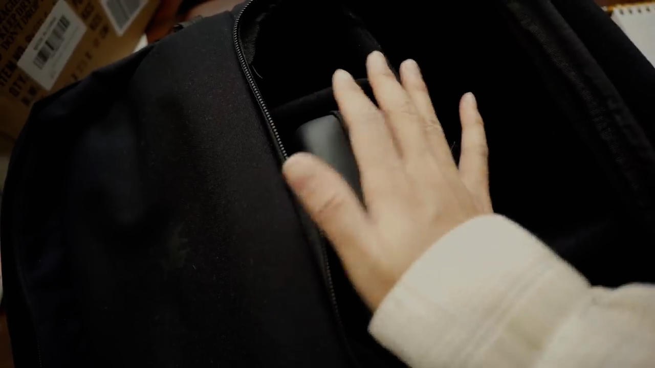 a closeup view of a person's hand reaching into a black backpack. the backpack appears to be made of a durable fabric, and the hand is seen grasping something inside.