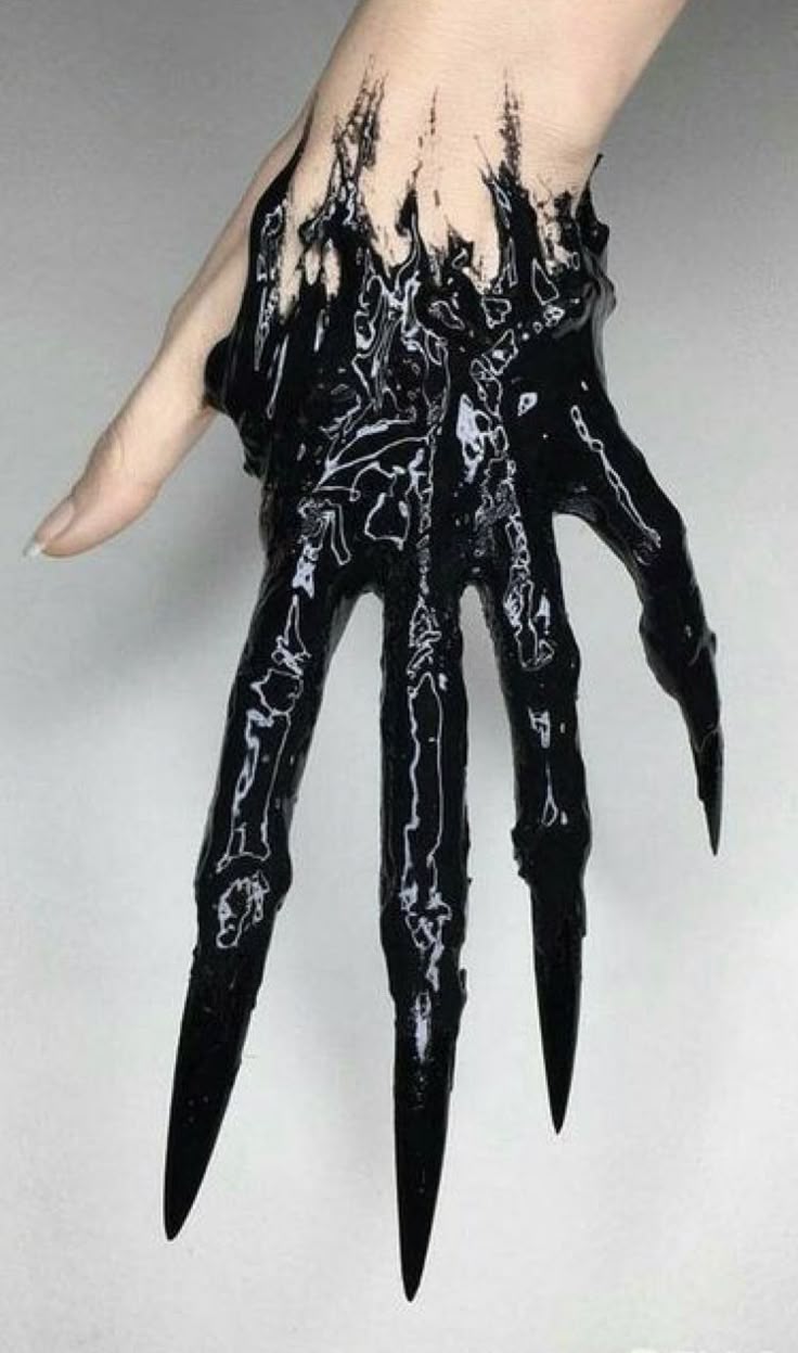 a hand covered in black paint, with sharp, elongated fingernails resembling claws, against a white background. the paint is thick and glossy, appearing to drip down the hand.
