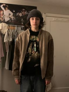 a young boy in a gray beanie and brown bomber jacket stands in a room looking at the camera.