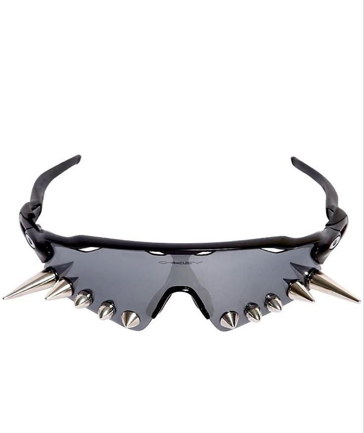 a pair of grey oakley sunglasses with a black frame are adorned with silver spikes along the bottom edge of the lenses. the spikes are of varying sizes, and the style is reminiscent of punk or avantgarde fashion.