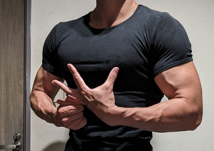 closeup image of a muscular man's torso and arms. he is wearing a black tshirt and is making a hand gesture with his fingers spread. his welldefined biceps and triceps are clearly visible, along with prominent veins. the man appears to be posing for a selfie in a mirror. the background is a plain wall. the overall impression is of a healthy and athletic physique.