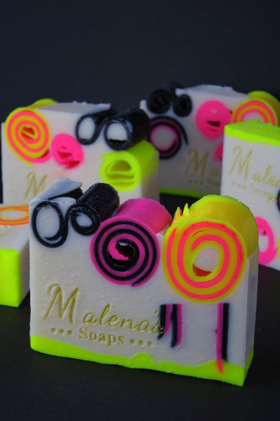 this is a closeup image of several bars of colorful handmade soap. the soap is made with a white base and decorated with swirls of black, yellow, pink, and lime green. the soap bars are arranged in a row, with the lime green bar at the front. the soap is labeled "malena's soaps." the image evokes a sense of luxury and pampering.