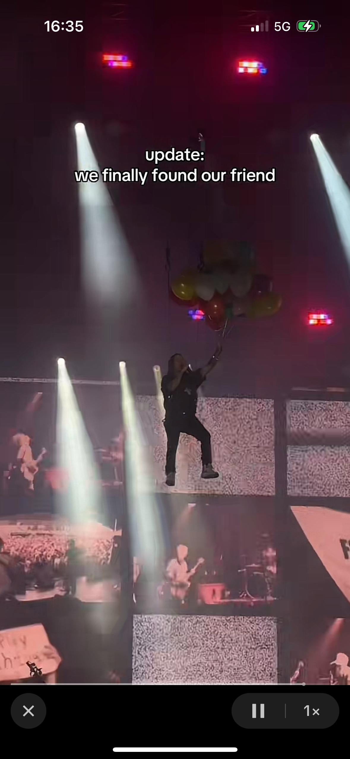a concert stage with a performer in the center surrounded by the audience and spotlights. the performer is holding a microphone and dancing in the spotlight. in the background, there is a big crowd and the stage is decorated with colorful balloons. the text overlay says "update: we finally found our friend."