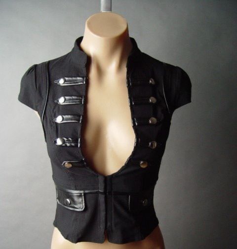 a close up shot of a black cropped jacket with silver buttons on a mannequin. the jacket is fitted and sleeveless, with a plunging neckline that shows cleavage. it has a collar and a faux leather trim. the mannequin is standing against a gray background.