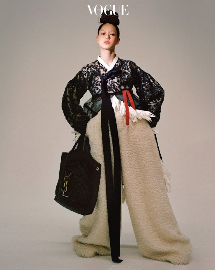 a fashion editorial image from vogue shows a woman in a fusion of traditional korean attire and modern elements. she is wearing a black lace top resembling a hanbok jacket, paired with widelegged fur pants. she is carrying a black quilted yves saint laurent handbag. the woman has a high bun hairstyle and a confident pose. the vogue logo is visible at the top of the image.