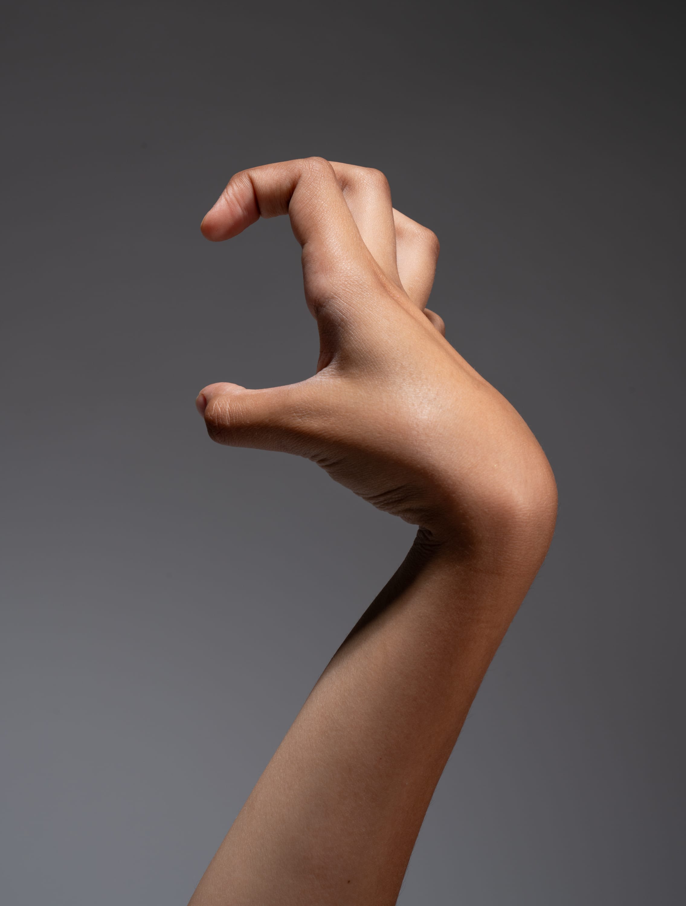 a closeup image of a hand with light brown skin, making a clawlike gesture against a neutral gray background. the hand is reaching forward as if grasping at something.