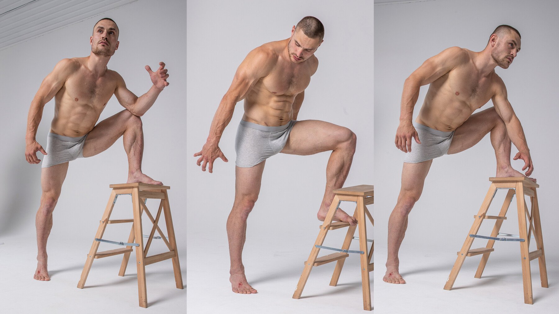 a shirtless, muscular man poses for a portrait in a studio setting. he is standing on a stool with one leg bent and his arms extended in different directions. he is wearing boxer briefs and has a strong, athletic build. the white background and simple lighting create a clean and professional feel. the image is a study in anatomy and movement.