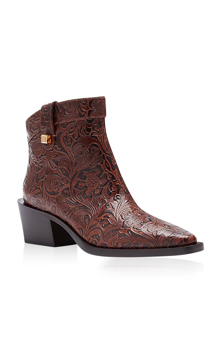 a pair of brown leather women's ankle boots with a pointed toe and a block heel are displayed against a white background. the boots are embossed with a floral pattern.