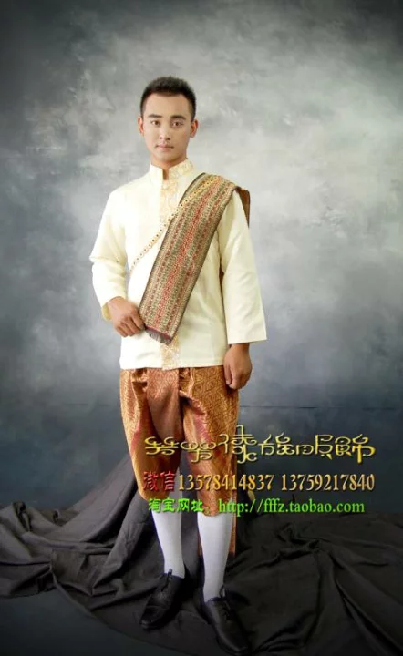 a young asian man is standing in a studio against a light grey background. he is wearing a white traditional thai outfit. his longsleeved white shirt is embellished with a gold trim. he is wearing a gold and brown silk sash, a traditional thai garment. the sash is draped diagonally across his body and tied at his waist. he is also wearing a pair of brown shoes and white socks. the man is smiling at the camera. there is a dark grey cloth under the man. the caption on the image is "traditional thai clothing." the text also includes a phone number and website address.