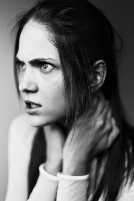 a black and white portrait of a woman with long, dark hair. she has a serious expression on her face and is looking at the camera. the lighting is dark and dramatic, highlighting her features. the focus is on her face and eyes, which show intensity and thoughtfulness.