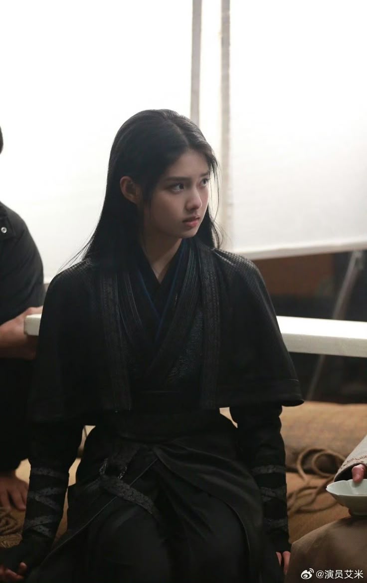 a young asian woman wearing a black costume, likely an actress named ai mi, sits looking off to the side.