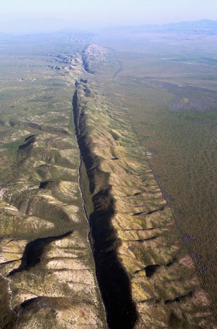 an aerial view of a vast desert landscape. in the center of the image, a deep canyon cuts through the land, creating a dramatic geological formation. the canyon is surrounded by rugged mountains, indicating a significant tectonic activity. the image shows a wide, barren landscape under a clear sky.