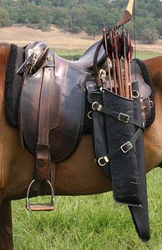 the image shows a closeup view of a horse's back, highlighting a traditional leather saddle and a black leather quiver filled with arrows. a recurve bow is also attached to the quiver. the horse is standing on a grassy field, bathed in natural sunlight. the overall aesthetic suggests a connection to horseback archery or traditional equestrian practices.