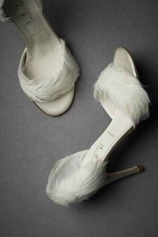 two white high heel shoes adorned with white feathers are displayed against a gray background.