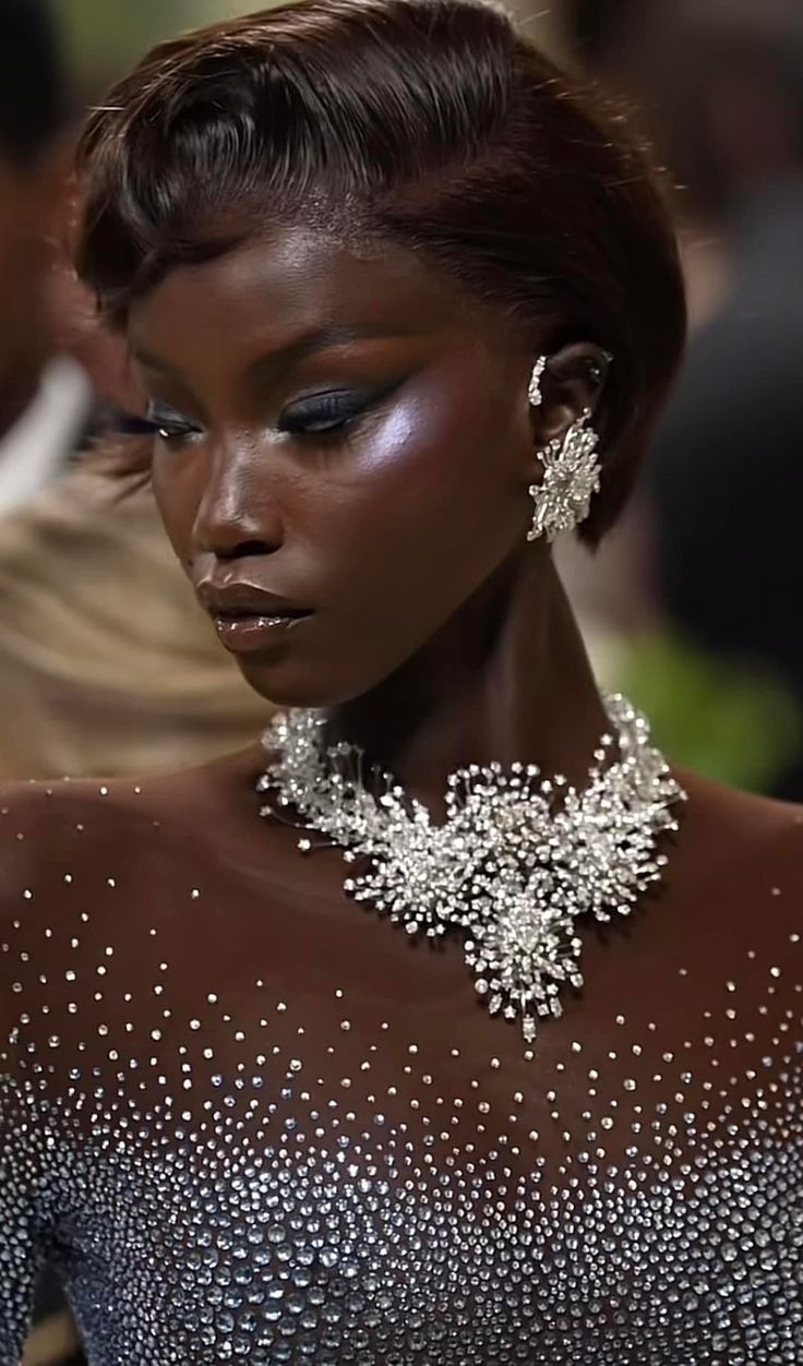 the image is a closeup portrait of a black woman, possibly a model,  wearing a stunning, darkcolored, sequinencrusted gown. she has short, dark brown hair styled in a sleek, sophisticated updo. the woman is adorned with a large, extravagant diamond necklace and matching earrings. her makeup is subtly glamorous, highlighting her high cheekbones and dark eyes.  the overall impression is one of elegance, high fashion, and beauty.  the background is blurred but suggests a highend event setting, possibly the met gala.