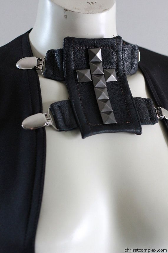 closeup of a black leather garment accessory featuring a studded cross design and clasps. it is displayed on a mannequin.