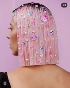 a closeup image of a young woman with short pink hair styled in a bob haircut. the hair is decorated with colorful pearl and rhinestone stickers, creating a fun and trendy look. her skin is fair and her expression is calm. she looks away from the camera.