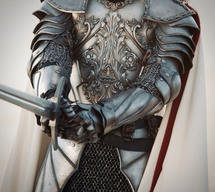 the image is a closeup shot of a knight clad in meticulously detailed, silvertoned plate armor.  the armor is highly ornate, featuring intricate carvings and flourishes.  chainmail is visible beneath the plate armor on the arms and around the waist. the knight holds a sword, and a portion of a white cloak or surcoat with a red trim is visible behind the armor. the overall impression is one of power, elegance, and historical significance, possibly suggesting a fantasy or historical setting. the image focuses primarily on the knight's upper body and arms, showcasing the artistry and craftsmanship of the armor.