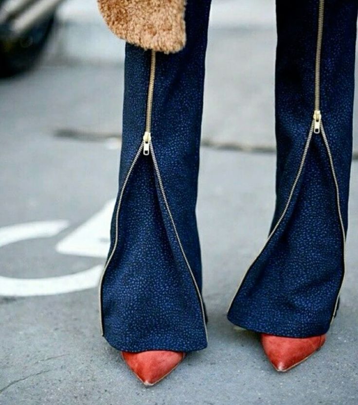 a woman is wearing dark blue jeans with two zippers down each leg, and red high heels. the jeans are fitted and the heels are a classic style. the woman's legs are crossed at the ankles.