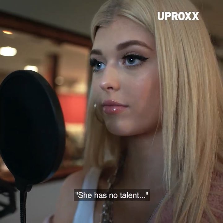 a closeup shot of loren gray in front of a microphone with a pop filter, likely in a recording studio. the text overlay reads "she has no talent...". the uproxx logo is in the upper right corner. gray is wearing a white tank top and a light pink cardigan, with a silver chain around her neck. she has blonde hair, blue eyes, and makeup including eyeliner and lip gloss.