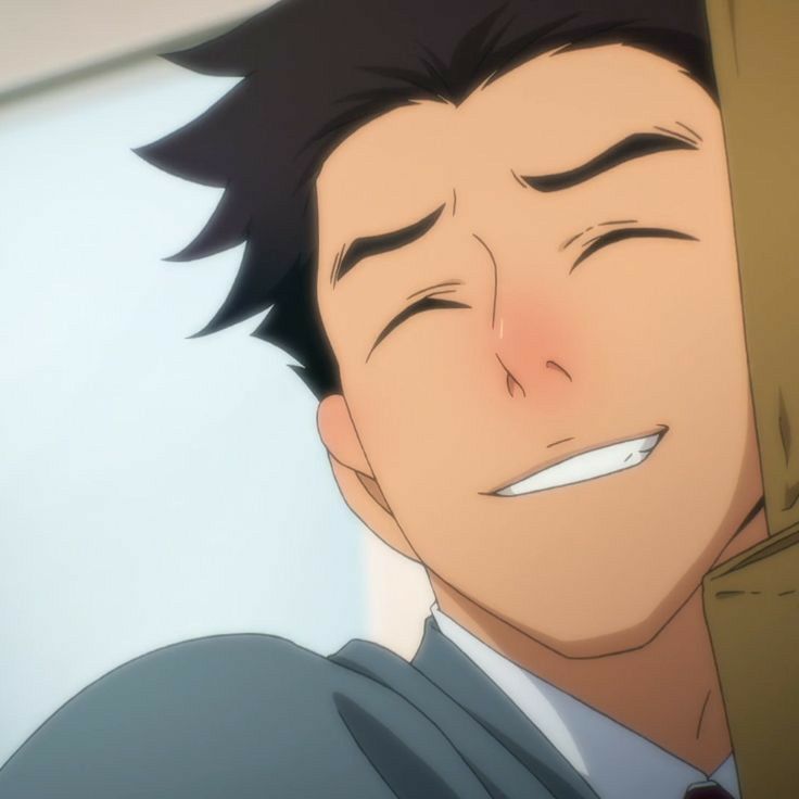 a close up shot of an anime character's face. he is smiling brightly, his eyes closed and his cheeks flushed. his hair is brown and his eyes are a deep brown, he is wearing a suit and tie. the background is blurred out, it looks like he is indoors.
