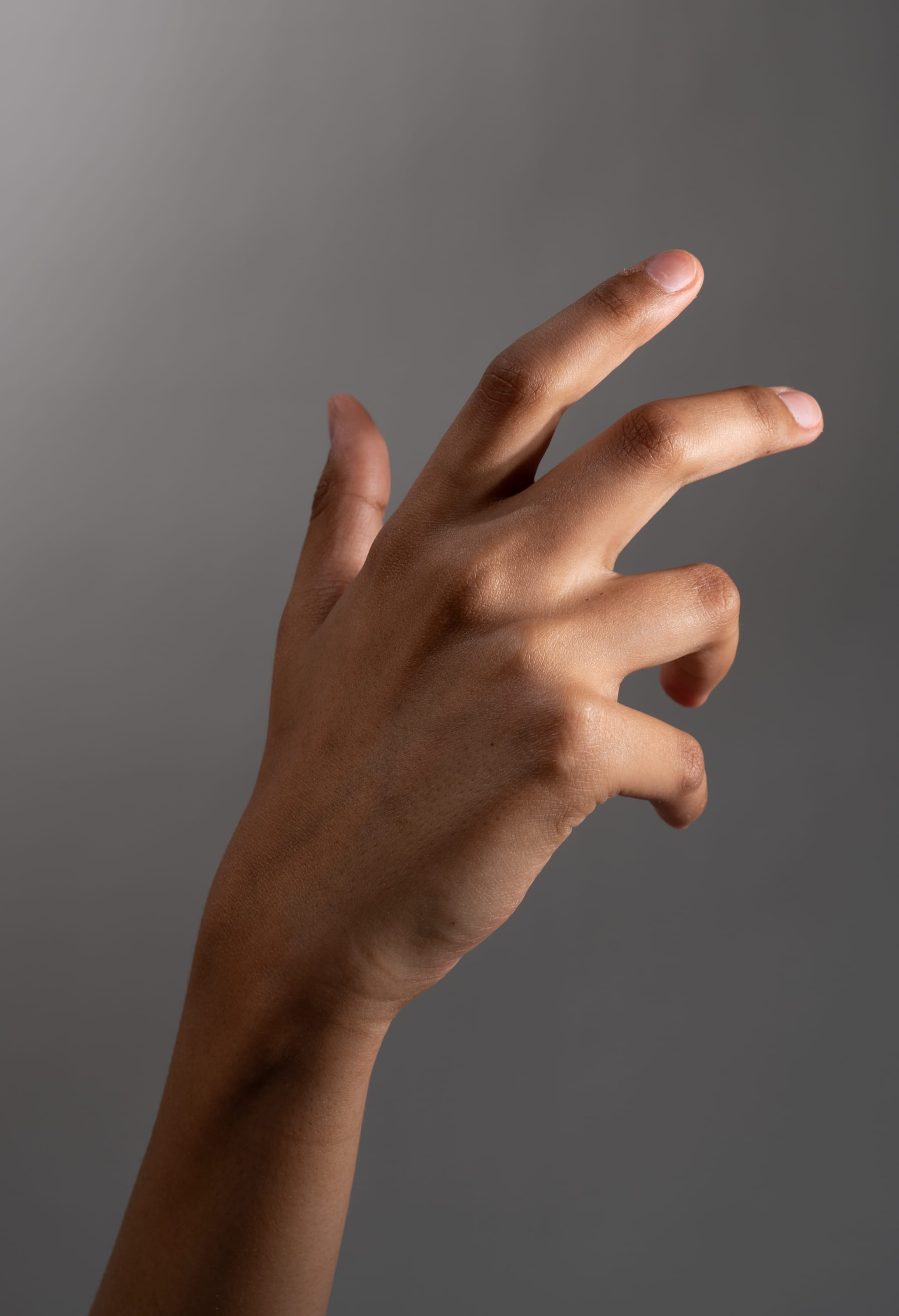 a hand is extended with the fingers curled inward, set against a neutral gray background. the lighting highlights the texture and contours of the skin.